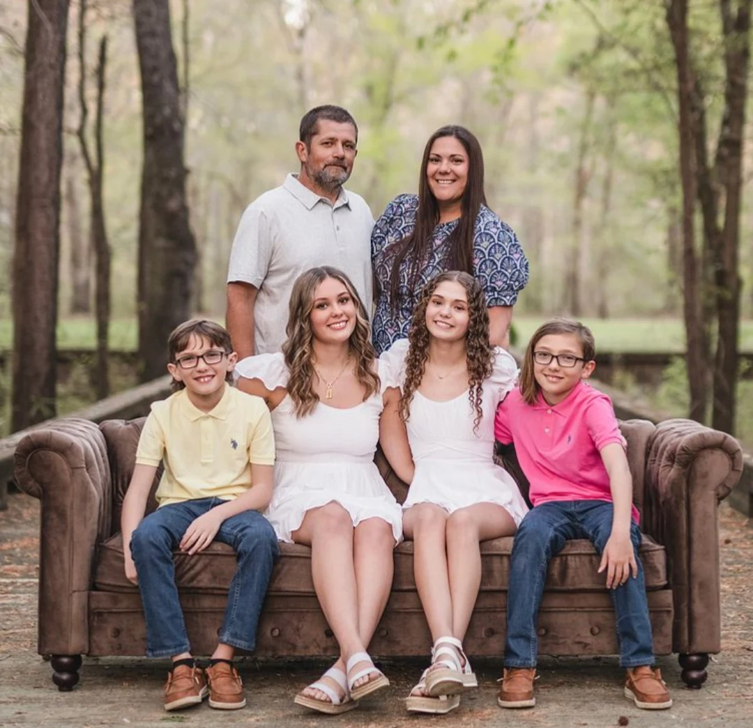 Cathrine Skipper with her husband, their two daughters and their twin boys, seated on a brown sofa outdoors among trees